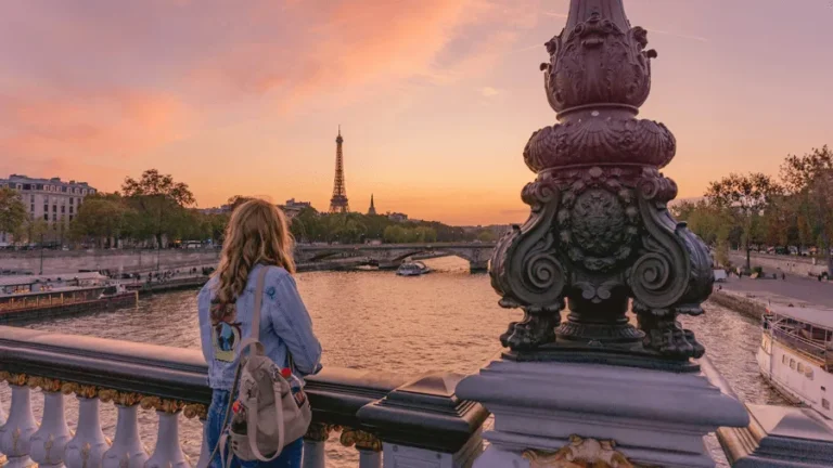 Kvinna på bro som tittar på solnedgång i Paris.