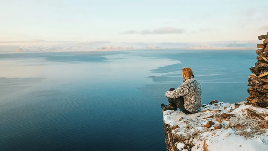 En man som sitter på en klippa och blickar ut över Svalbards landskap.