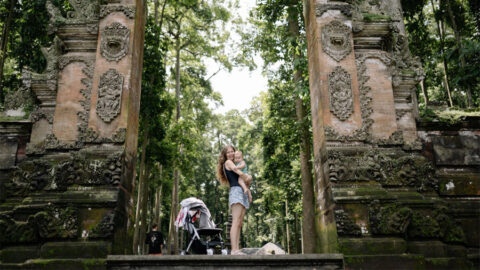 Kvinna med barnvagn vid tempelruin på Bali.