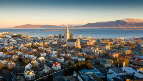 Utsikt över Reykjavik med Hallgrímskirkja, havet och fjällen i kvällsljus.