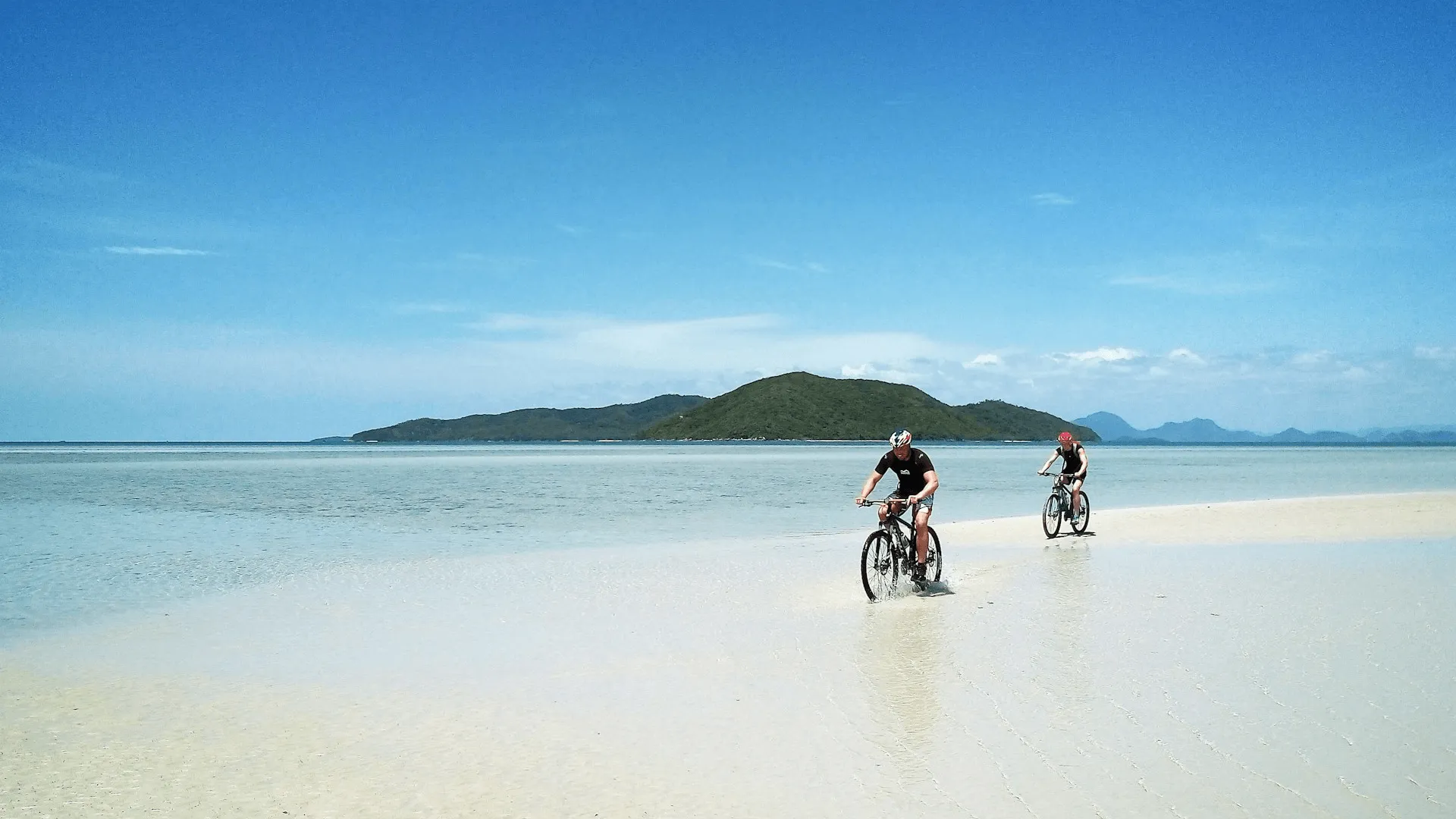 Två personer som cyklar på en strand i Koh Samui.