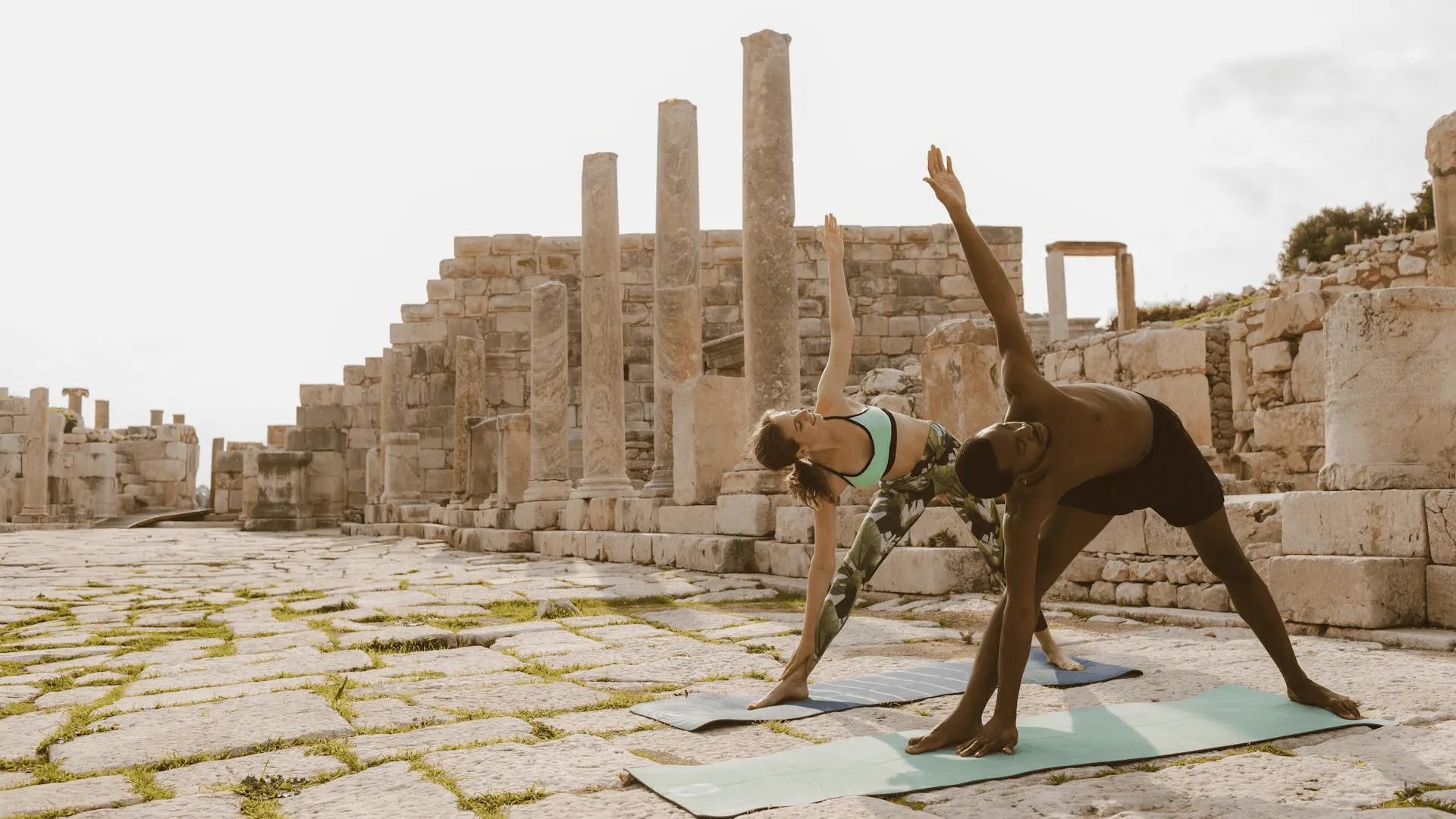 Två personer som utövar yoga i Grekland vid historisk monument.