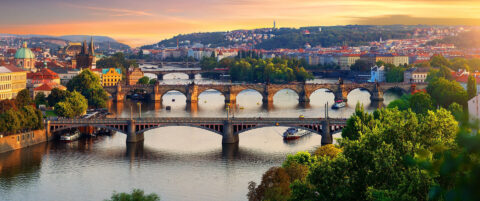 Panorama över Moldau i Prag i kvällsljus med Karlsbron och flera broar i rad, Gamla stans röda tak och tornsiluetter i bakgrunden