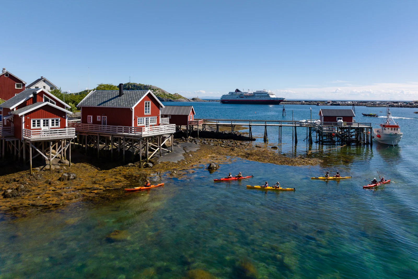 Röda rorbuer på pålar vid vattnet i Lofoten med kajakpaddlare utanför