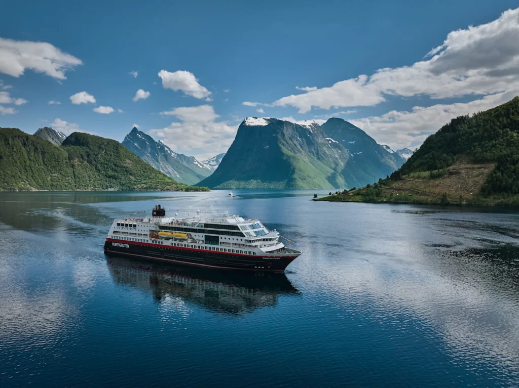 Hurtigrutens fartyg MS Trollfjord på väg genom Hjørundfjorden med branta fjällsidor på båda sidor