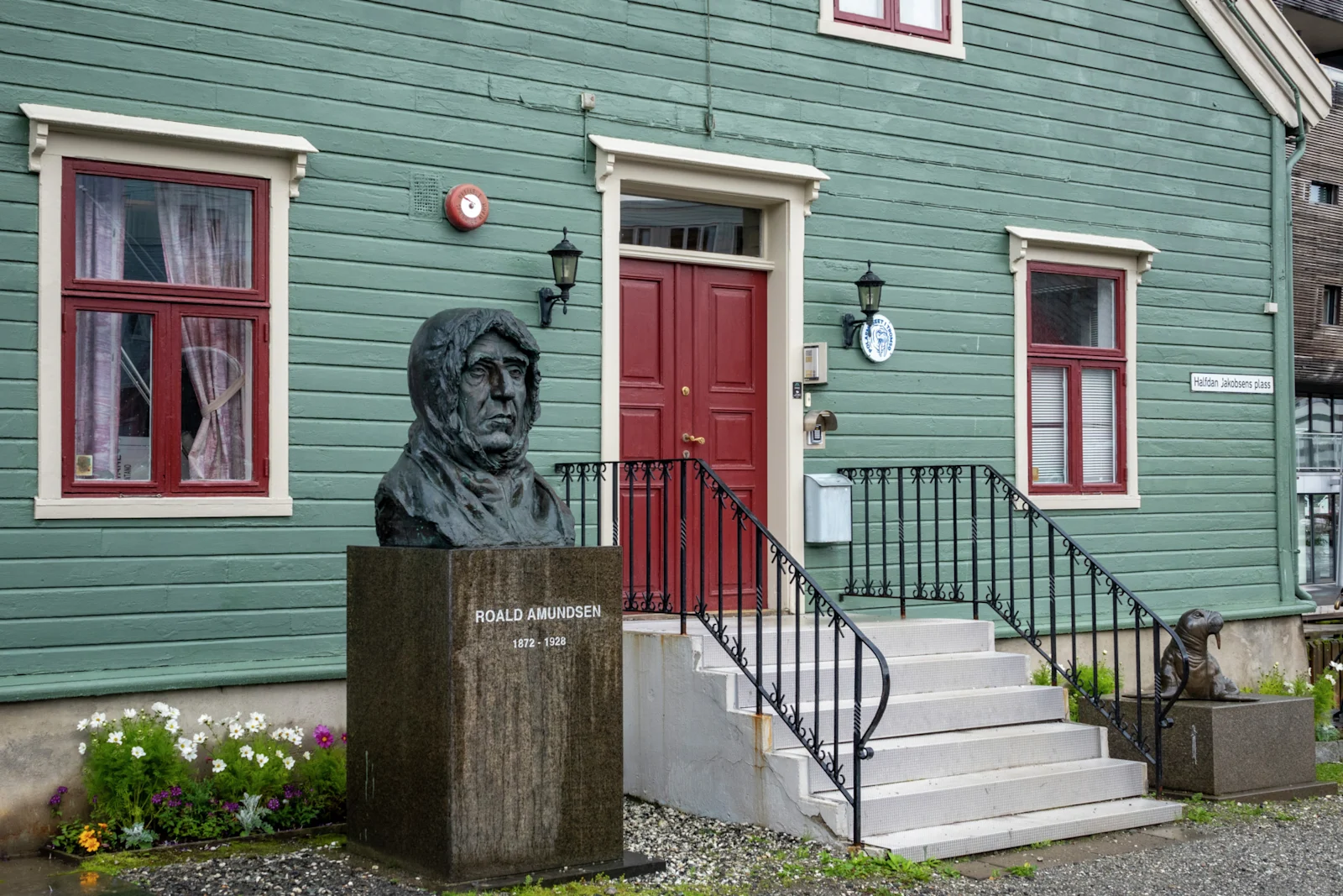 Byst av Roald Amundsen framför ett grönt trähus i Tromsö