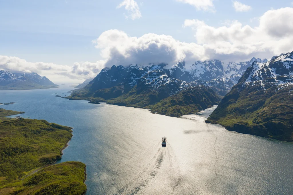 Flygbild över en fjord mellan snöklädda fjäll med ett fartyg på väg inåt