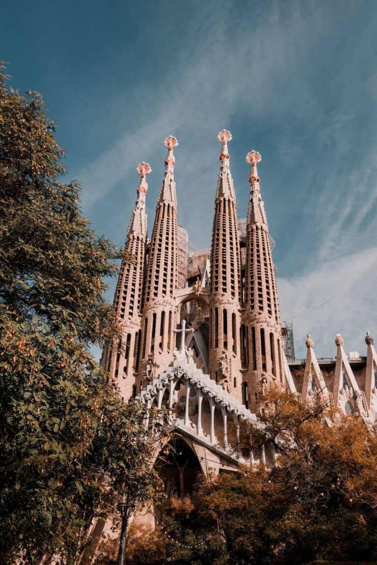 Sagrada Famílias fasad i Barcelona mot blå himmel, omgiven av träd