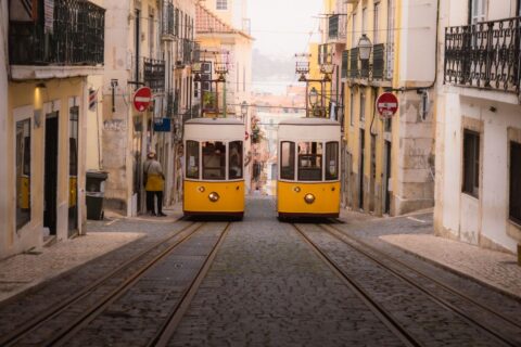 Två gula spårvagnar möts i en brant kullerstensgata i Lissabon