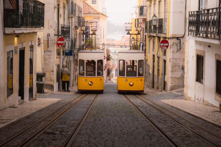 Två gula spårvagnar möts i en brant kullerstensgata i Lissabon