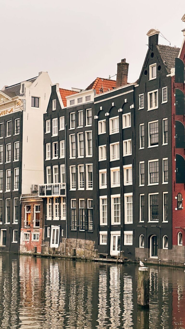 Historiska kanalhus med trappgavlar speglar sig i en kanal i Amsterdam