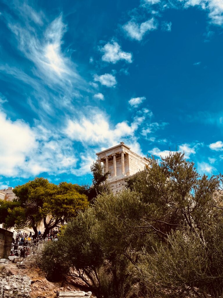 Athena Nike-templet på Akropolis i Aten mot blå himmel, omgivet av olivträd