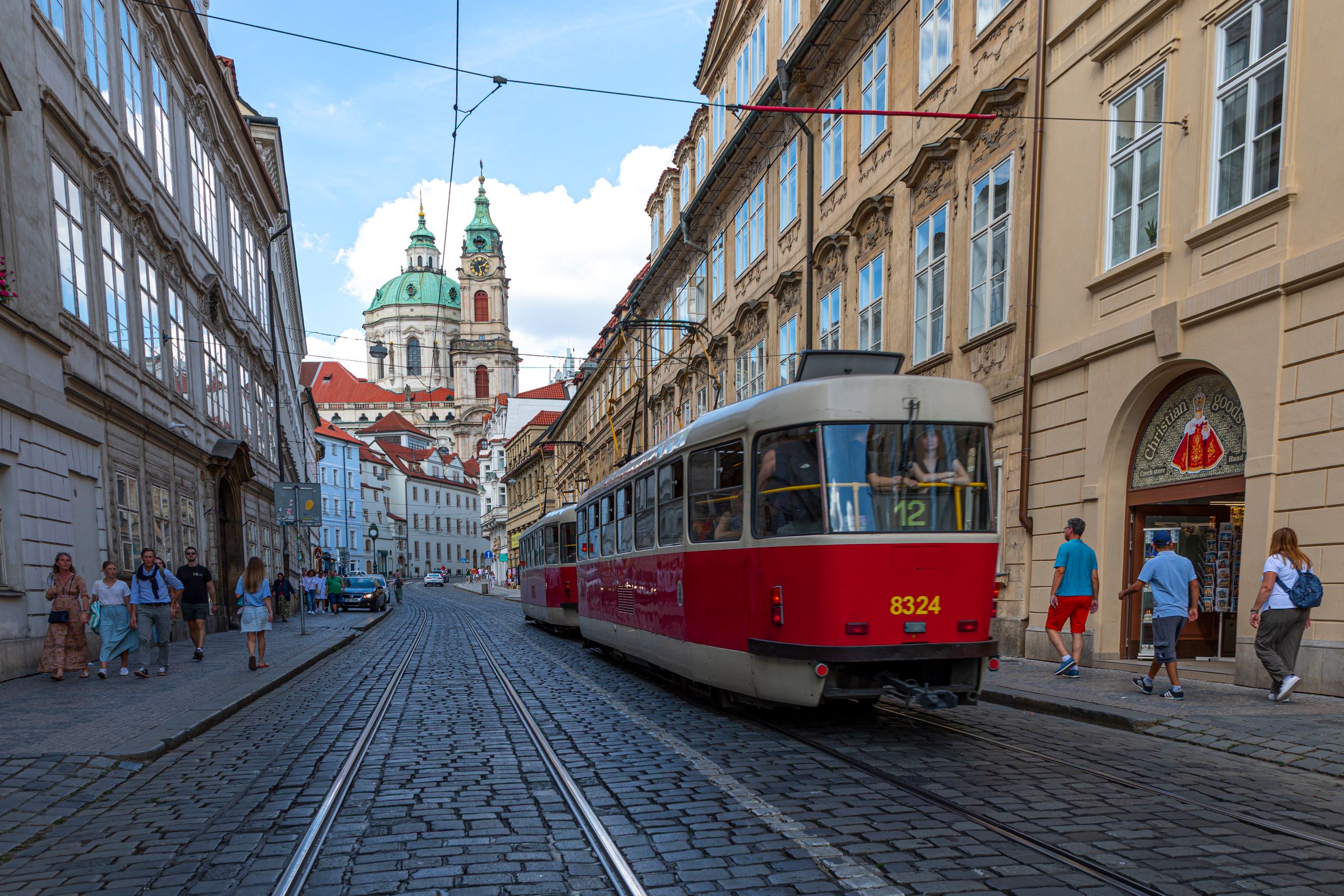 Röd spårvagn på en kullerstensgata i Malá Strana i Prag med Nikolaikyrkan i bakgrunden